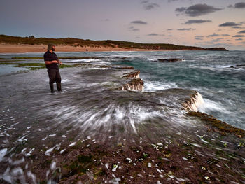 Rear view of man standing on beach against sky during sunset