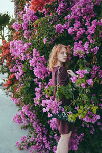 Portrait of beautiful young woman standing by pink flowering plants