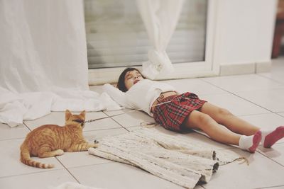 Girl sleeping with cat on tiled floor at home