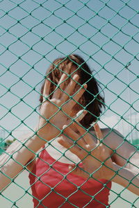 Woman touching net while standing at court during sunny day