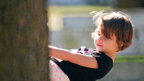 Side view of girl looking away by tree trunk