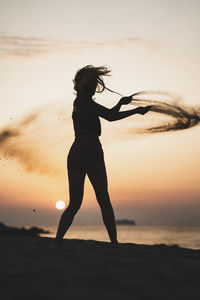 Silhouette woman standing on beach against sky during sunset