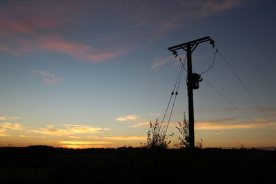 Silhouette electricity pylon on field against sky during sunset