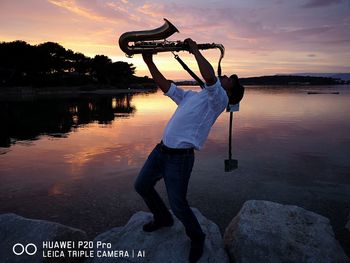 Man standing by lake against sky during sunset