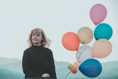 Portrait of woman with balloons standing against sky