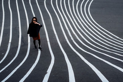Full length portrait of young woman standing on striped asphalt