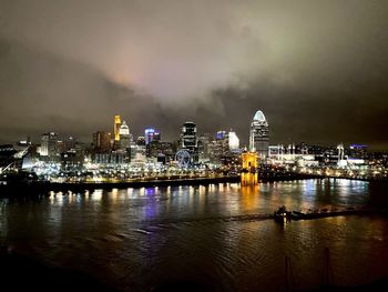 Illuminated buildings by river against sky at night