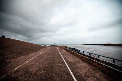 Empty road by sea against sky