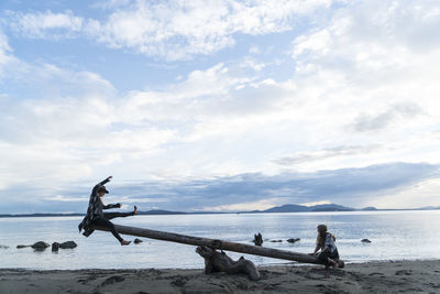 Two teenage girls using a a log as a seesaw on clayton beach