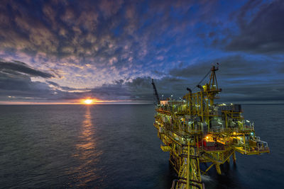 Drilling rig on sea against sky at sunset