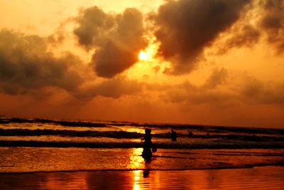 Silhouette people on sea against sky during sunset