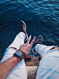 Low section of man gesturing peace sign while sitting on pier over sea