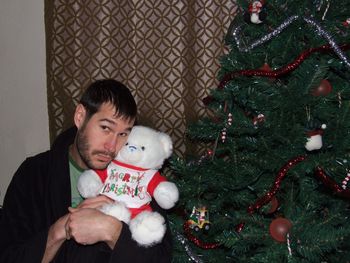 Man holding teddy bear while sitting by christmas tree