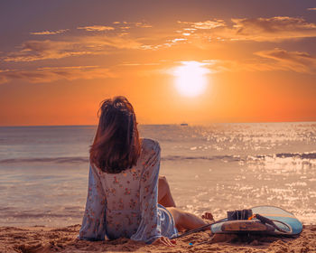 Rear view of woman sitting on beach during sunset