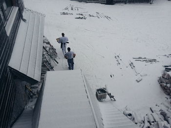 Rear view of people walking on snow covered field by house