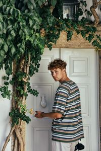 Side view of young man standing by christmas tree at home