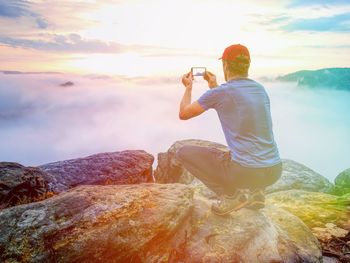 Man sit and takes phone photo of misty mountain valley. hiken in outdoor wearing. abstract light