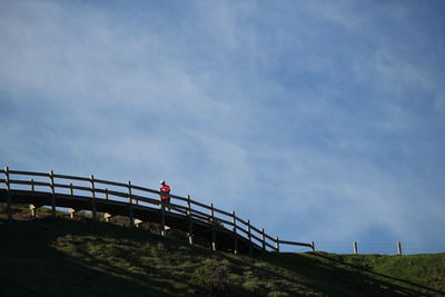 Low angle view of man walking on footbridge on hill against sky