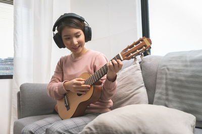 Young man playing guitar on sofa at home