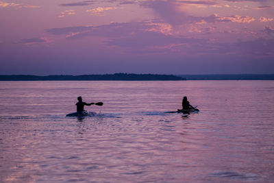 Silhouette people in sea against sky during sunset