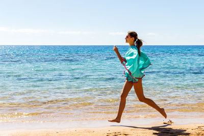 Full length side view of young woman running on shore at beach during summer