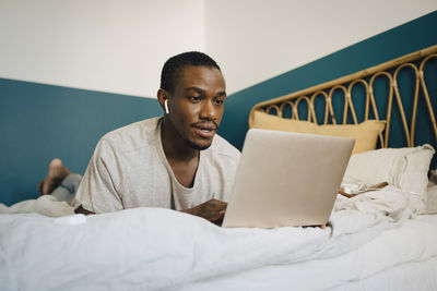 Mid adult man using laptop over bed in bedroom