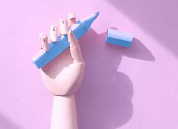 Cropped robotic arm holding blue felt tip pen against pink background