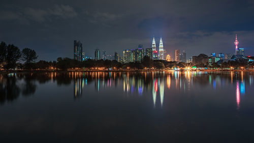 Illuminated buildings by lake against sky in city at night