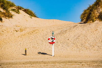 Arrow sign on sand against clear sky