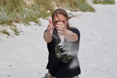 High angle view of mid adult woman throwing sand while standing at beach