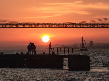 Silhouette people by sea against orange sky