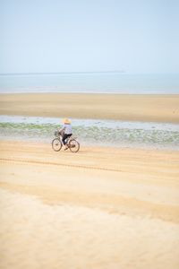 Person cycling on beach against sky