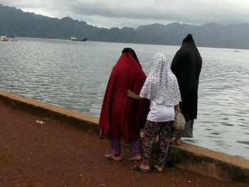 Rear view of women standing on shore against mountains