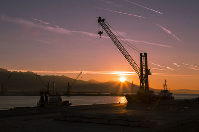 Silhouette cranes against sky at sunset