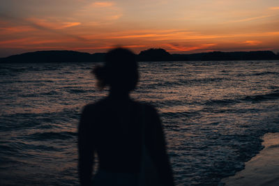 Silhouette woman standing at beach against sky during sunset