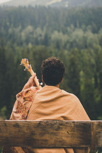 Rear view of man playing guitar sitting on bench