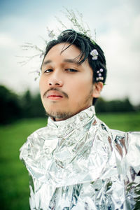 Close-up of a man wearing futuristic outfit and flower in his hair in a green field