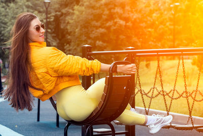 Side view of young woman sitting on yellow outdoors