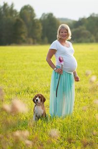 Portrait of pregnant woman standing with dog on grassy field