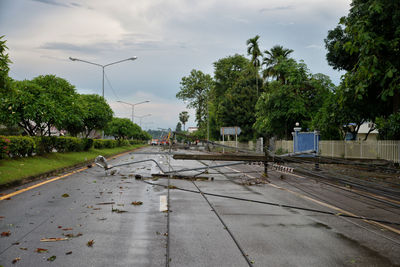 Wet road by trees in city against sky