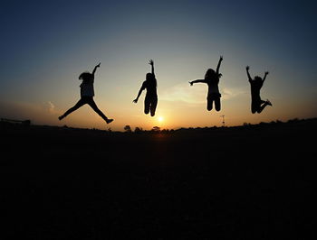 Silhouette people jumping on field against sky during sunset