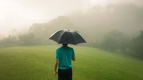 Rear view of man with umbrella standing on field against sky