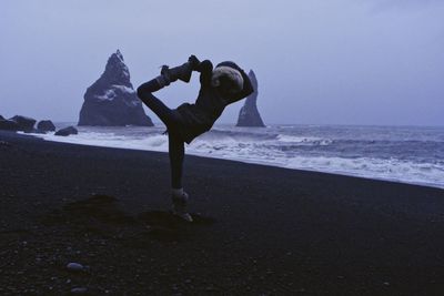 Woman practicing yoga at beach during winter