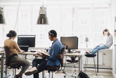 Male and female computer hackers working against window in creative office