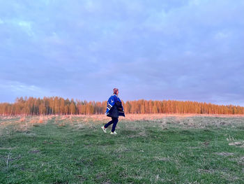 Rear view of man walking on field against sky