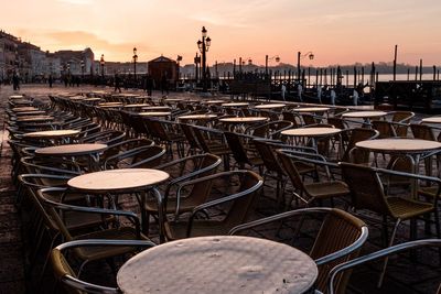 Empty chairs and tables against sky at sunset