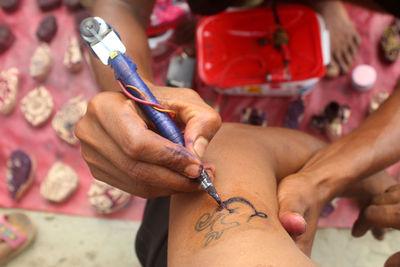 High angle view of hands making tattoo on customer