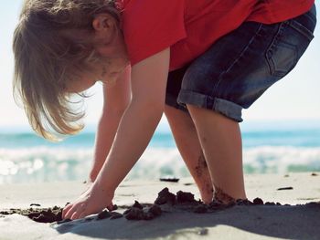 Side view of little boy playing on wet shore during sunny day