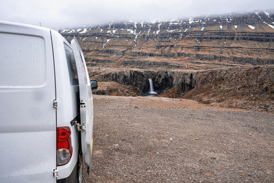 Van parked on cliff overlooking folaldafoss waterfall against mountain in valley