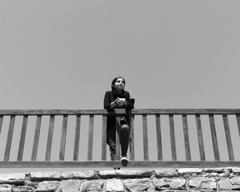 Portrait of young woman standing on railing against clear sky